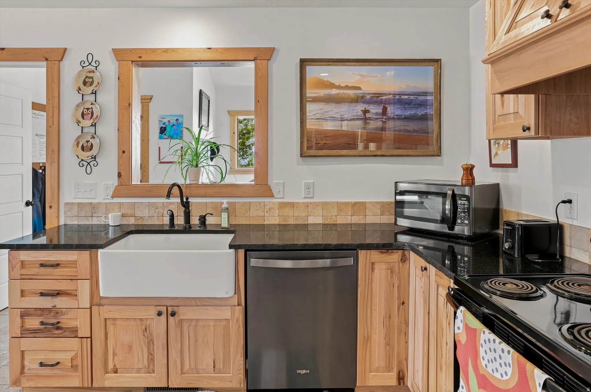 Kitchen featuring natural wood cabinetry, black countertops, and a white apron-front sink with a dark-finish faucet
