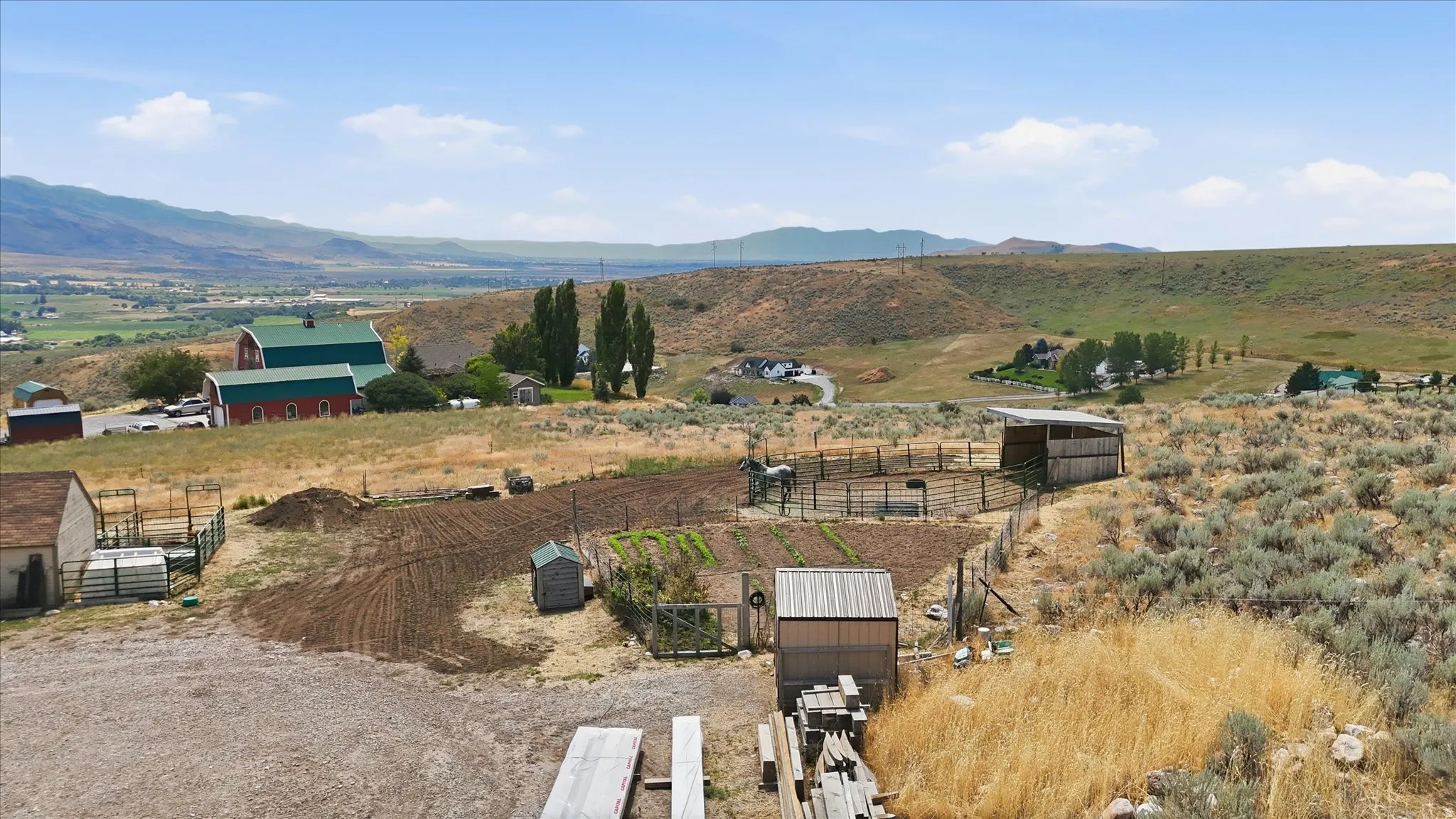 Expansive property featuring tilled garden beds, multiple outbuildings, and fenced animal enclosures