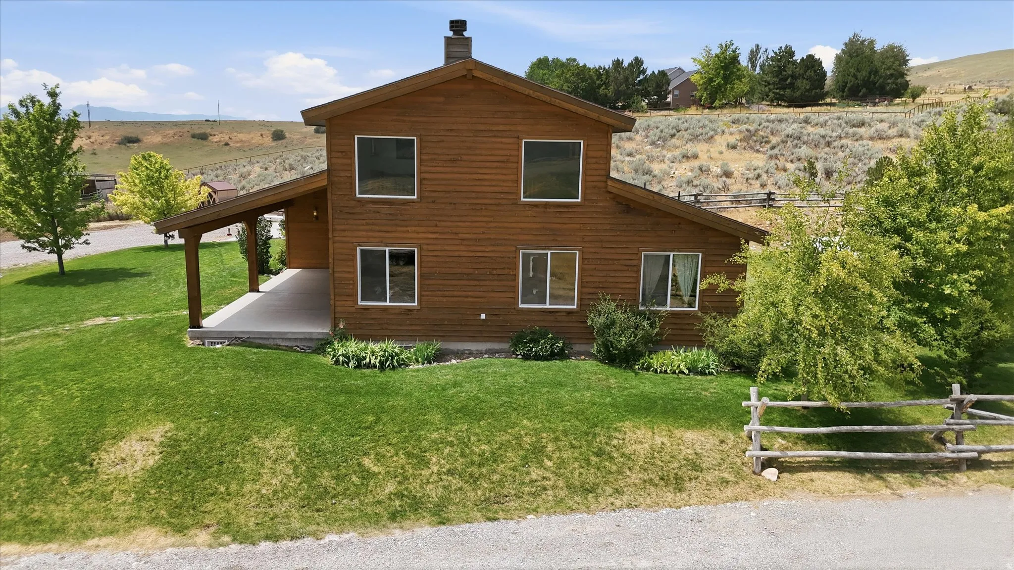 Wood-sided home featuring a covered porch, stone chimney, and a sloped lawn