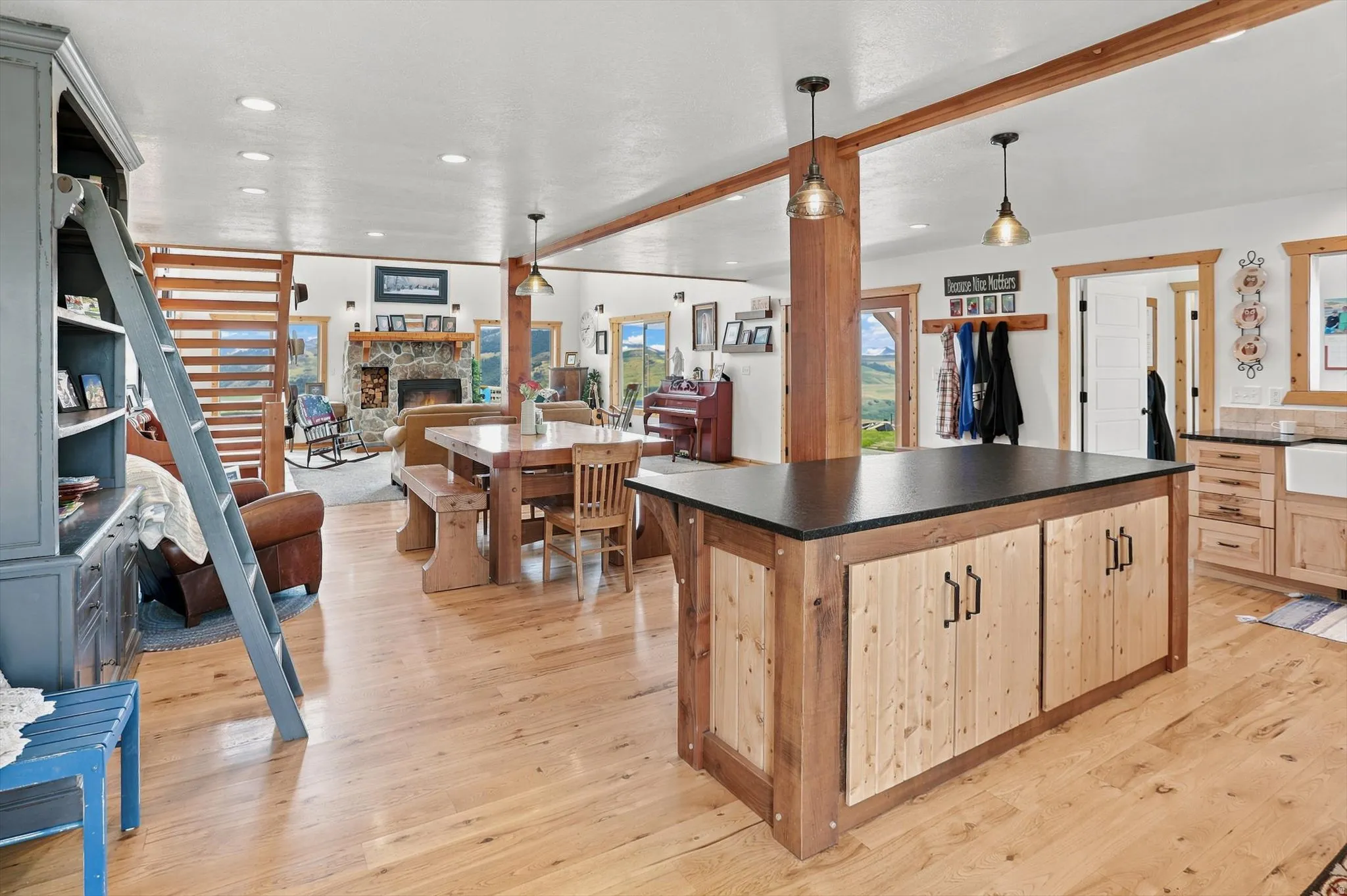 Open-concept living area with light wood-finish flooring, exposed wood beams, and recessed lighting