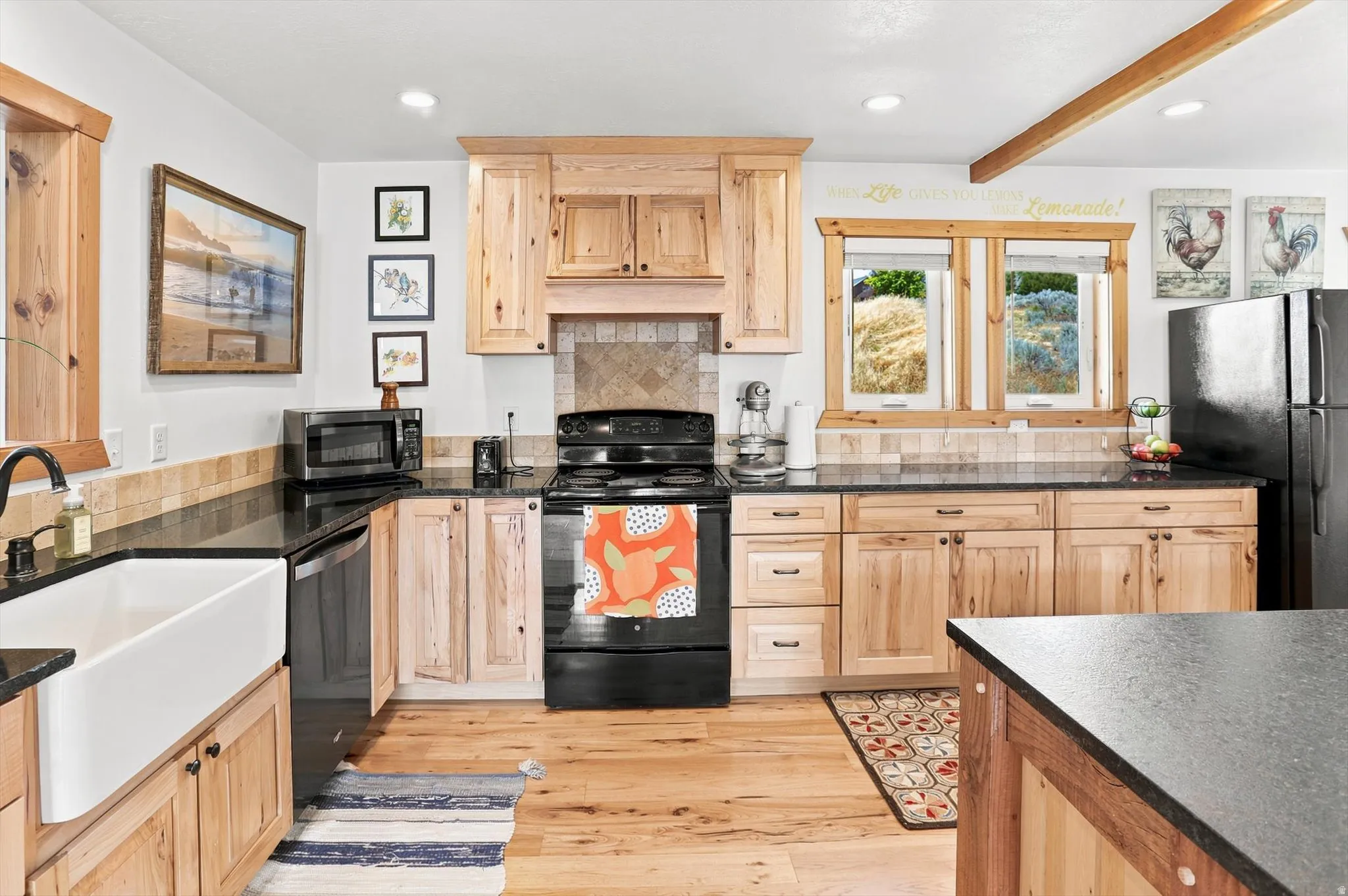 Kitchen featuring natural wood cabinetry, black countertops, a farmhouse sink, and black appliances