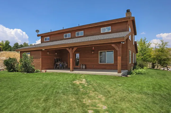 Wood-sided residence featuring a covered patio, multiple windows, and a stone pathway across the lawn