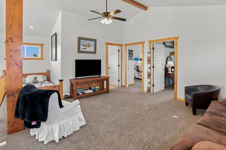 Carpeted loft area featuring vaulted ceilings with exposed wood beams