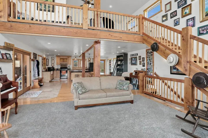 Open-concept living space with a high ceiling, exposed wood beams, and a light wood staircase leading to an upper-level balcony