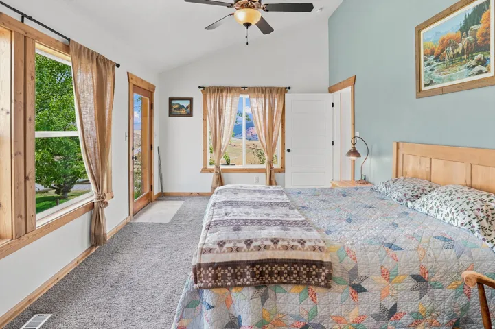 Primary Suite Vaulted ceiling room featuring light wood-finish trim, dark gray carpeting, and a ceiling fan with integrated lighting