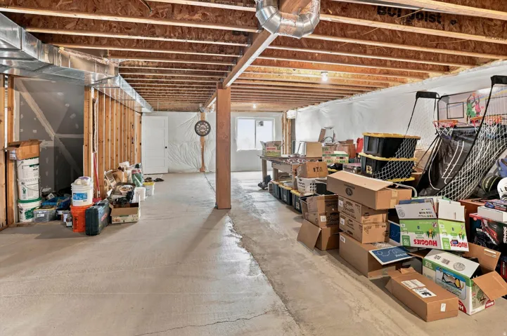 Unfinished basement featuring exposed joists, concrete flooring, foundational support beams, and visible ductwork