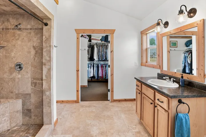 Primary Suite Bathroom featuring a walk-in shower with tile surround and integrated bench, wood-finish vanity with countertop and integrated sink, framed mirror, and wood-finish trim throughout