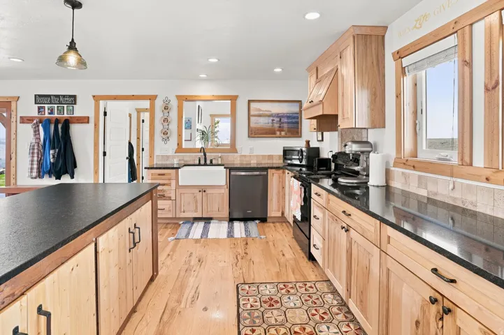 Expansive kitchen featuring light wood cabinetry, black countertops, and wood-finish flooring