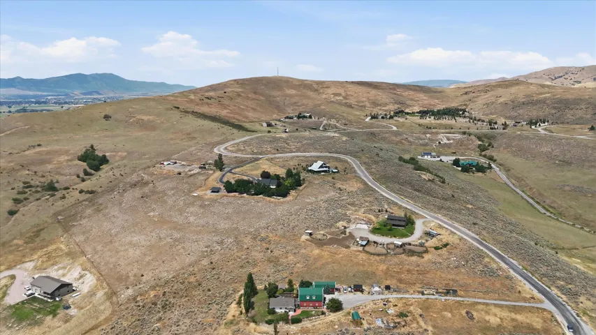 Expansive land parcel featuring undulating topography, a road, natural vegetation, distant mountains, and scattered residential structures