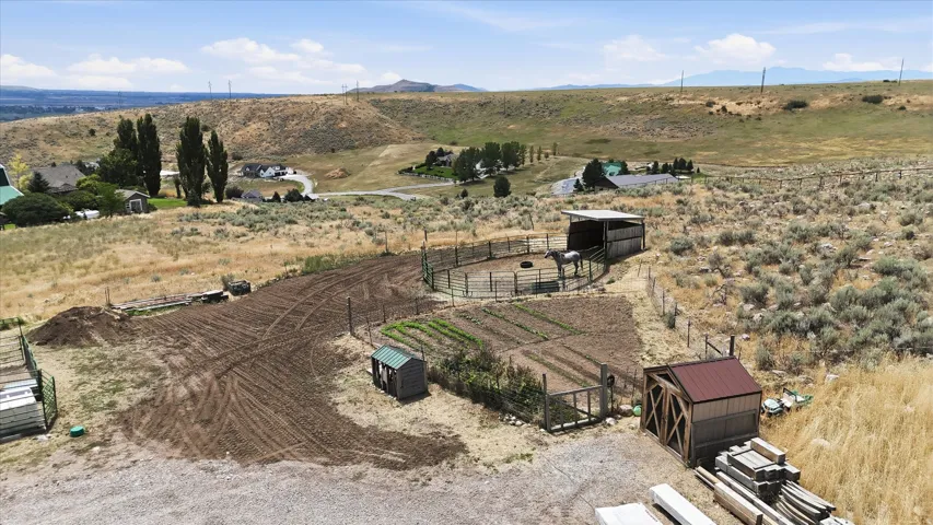 Expansive property featuring a circular fenced corral with an attached covered shelter, multiple garden beds, a smaller fenced enclosure, a compact shed with a green roof, and a larger shed with a red metal roof