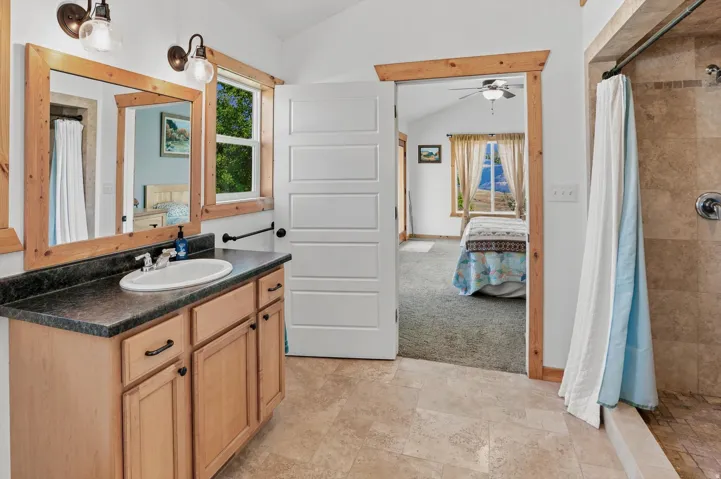 Primary Suite Bathroom featuring a wooden vanity with dark countertop, an oval undermount sink, and two framed mirrors, large step in shower
