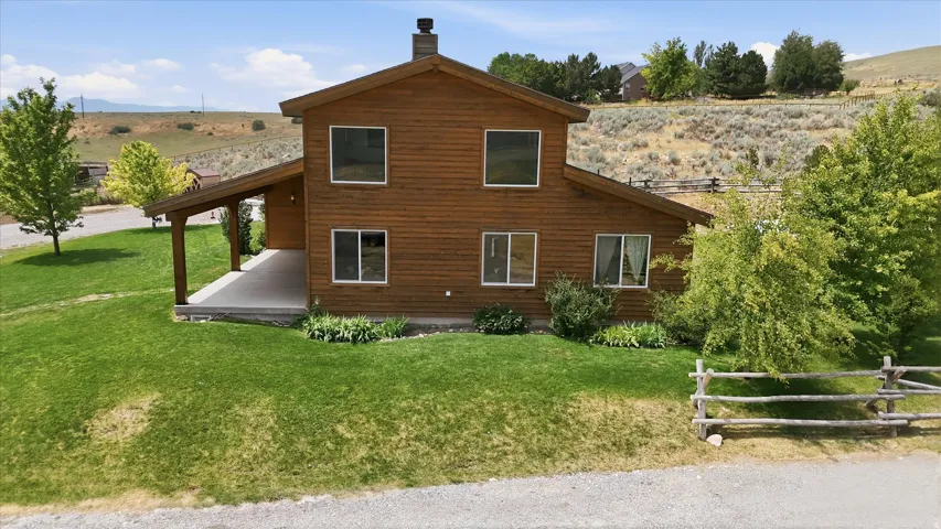 Wood-sided home featuring a covered porch, stone chimney, and a sloped lawn