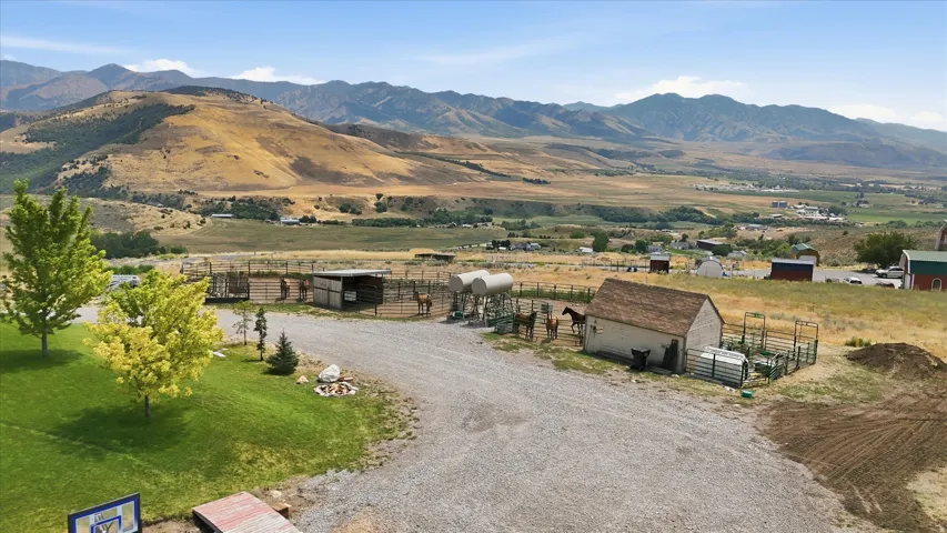 Expansive property featuring a gravel driveway, multiple fenced enclosures, and a detached outbuilding with a brown shingle roof