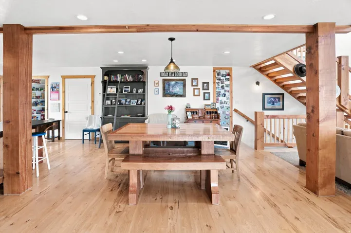 Open concept living space featuring wood-finish flooring, exposed wood beams, and a prominent wood staircase with matching railing