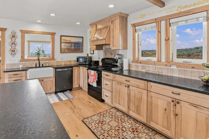 Well-appointed kitchen featuring wood-finish flooring, natural wood cabinetry, dark countertops, and a white farmhouse sink