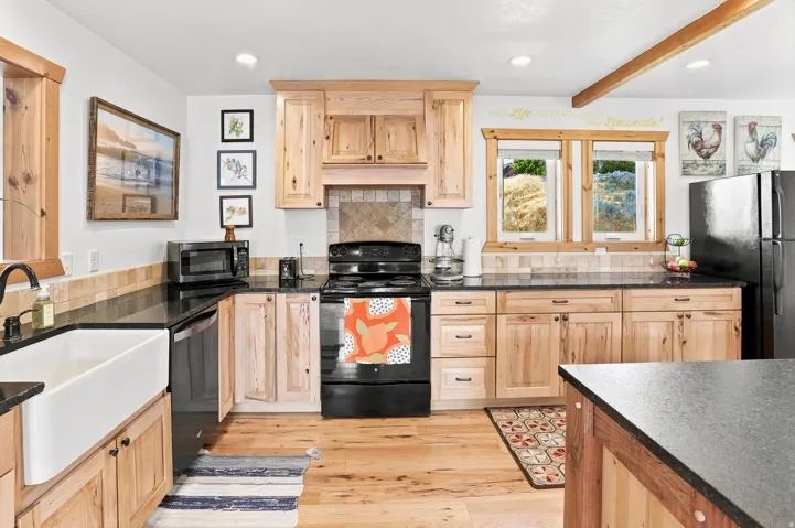 Kitchen featuring natural wood cabinetry, black countertops, a farmhouse sink, and black appliances