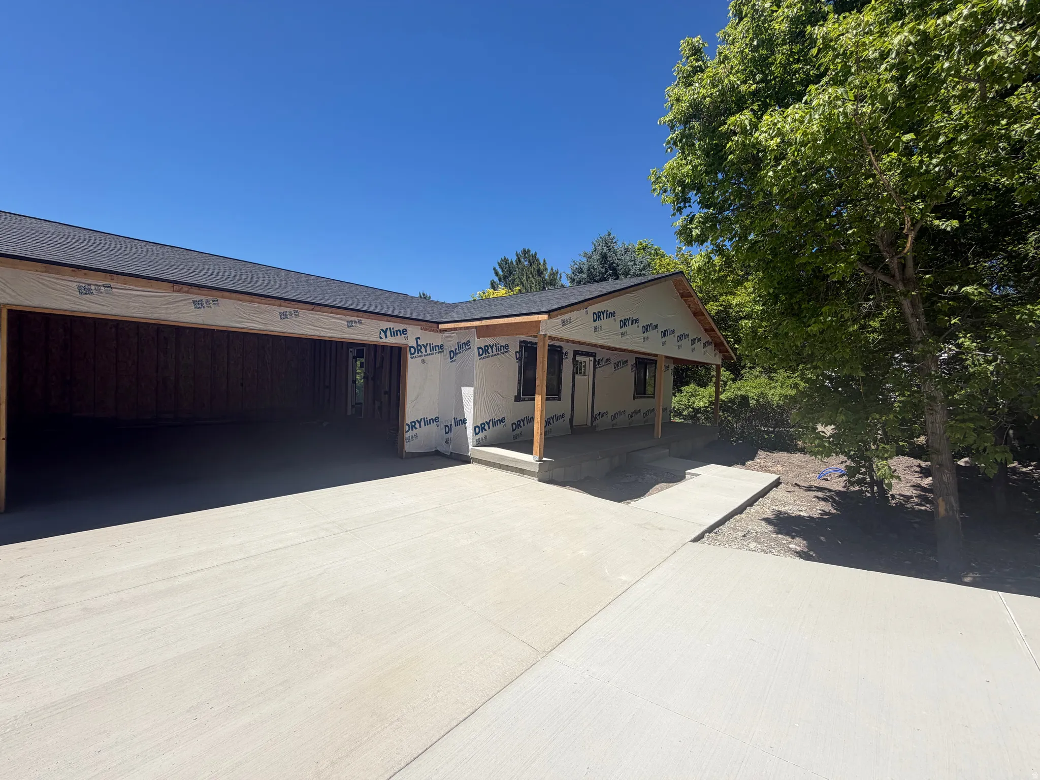 New construction framing featuring a covered entry, dark shingle roofing, and an attached garage with a concrete driveway