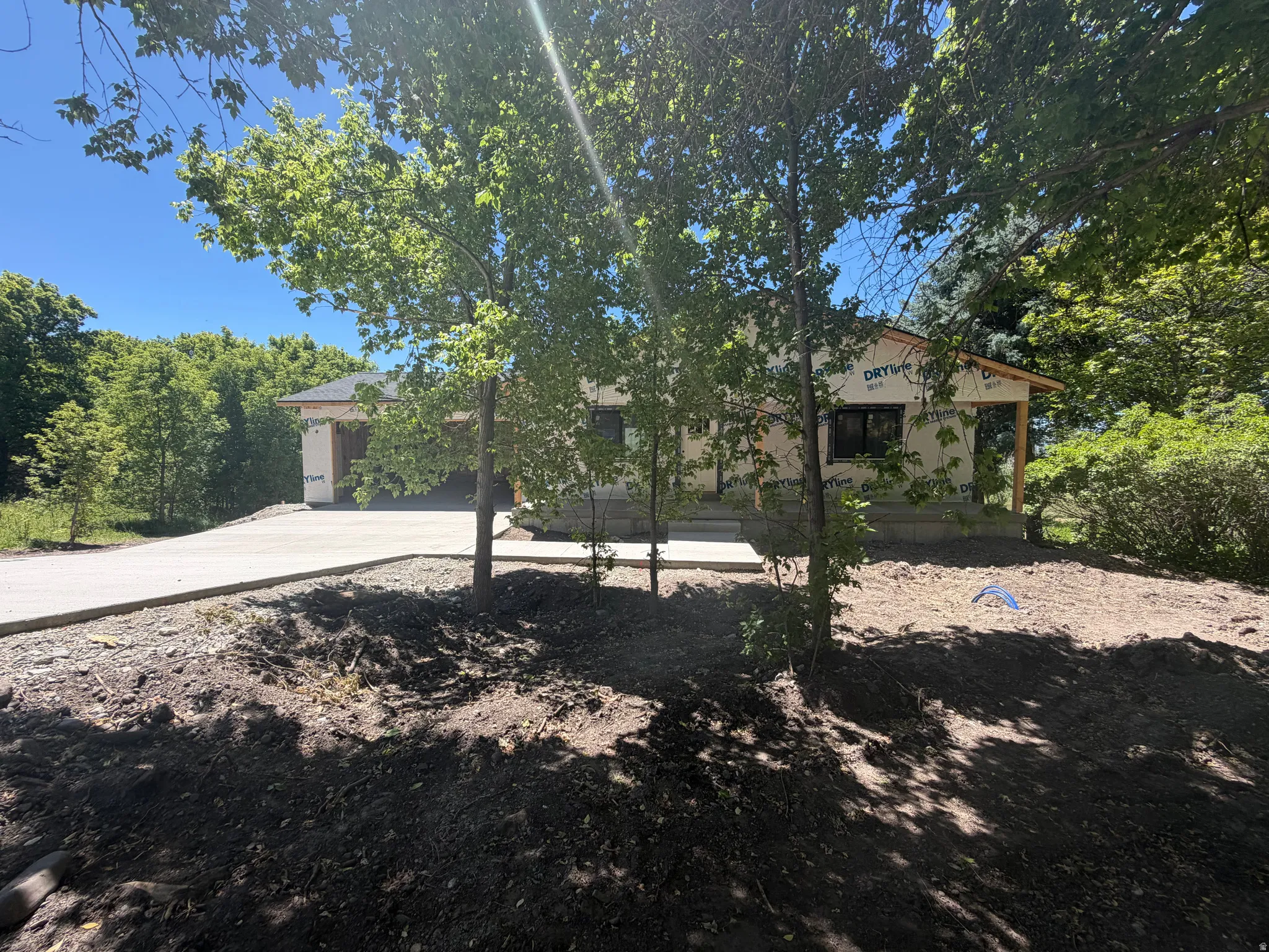 New construction home featuring a concrete driveway, wrap-around porch framing, and a wooded setting