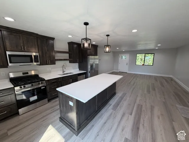 Contemporary kitchen with dark wood-finish cabinetry, stainless steel appliances, and a central island featuring a light-toned countertop