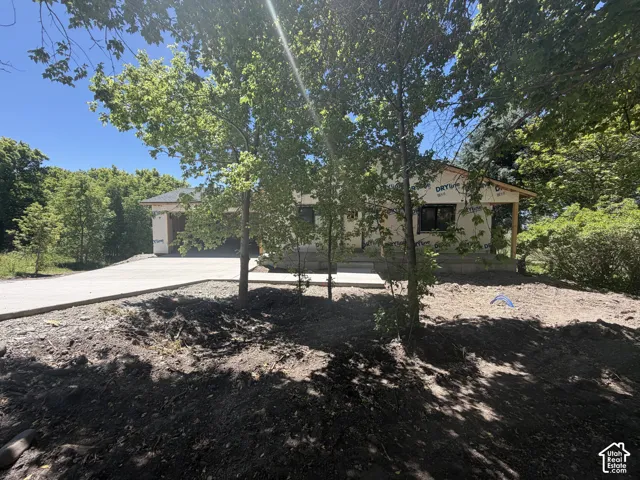 New construction home featuring a concrete driveway, wrap-around porch framing, and a wooded setting