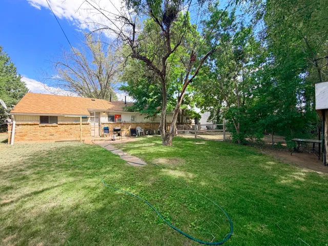 Expansive backyard featuring a manicured lawn, established trees, a brick-faced exterior, a shingle roof, and a concrete pathway