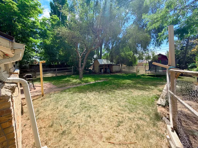 Spacious backyard featuring mature trees, a storage shed, and perimeter fencing