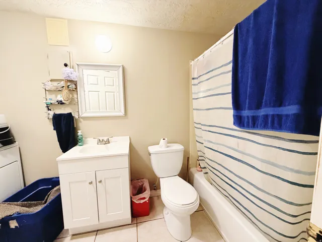 Full bathroom featuring a white vanity with integrated sink, a commode, and a tub-shower combination with a striped shower curtain