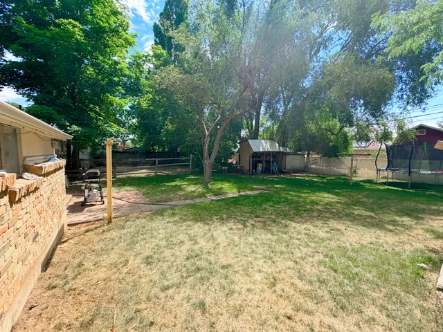 Spacious backyard featuring mature trees, a storage shed, and perimeter fencing