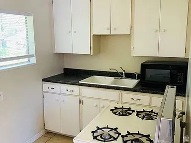 Kitchen featuring white cabinetry, dark countertops, a double-basin sink, a built-in microwave, and a white gas range with four burners