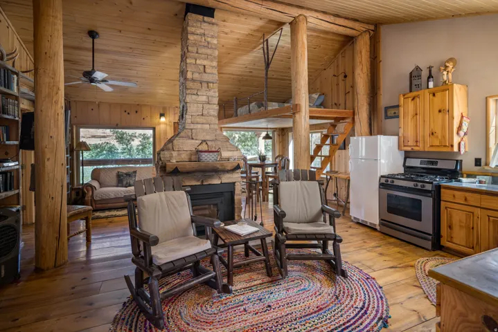 Open-concept living space featuring a floor-to-ceiling stone fireplace, exposed log columns, and wood-finish flooring