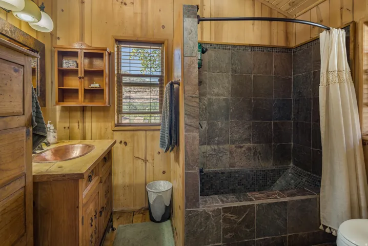 Bathroom featuring a wood-panelled interior, a copper vessel sink, a wood vanity, and a tiled shower with a mosaic-tiled bench