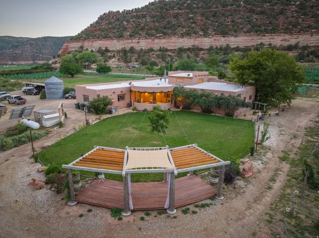 Expansive outdoor entertainment area featuring a circular wood-finish deck with a pergola, a large manicured lawn, and mature landscaping