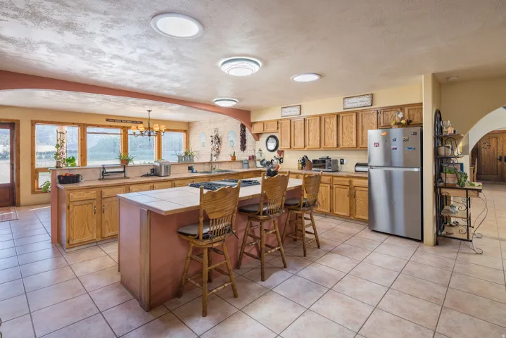 Spacious kitchen featuring a central island with a tile countertop, light wood cabinetry, stainless steel appliances, and a tile floor