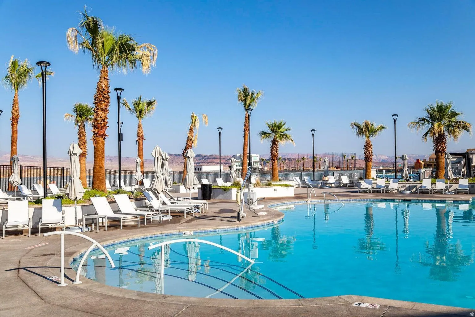 Resort-style pool area featuring a curved swimming pool, extensive deck space, multiple palm trees, and modern light posts