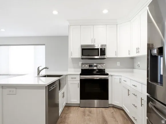 Modern kitchen featuring white cabinetry, stainless steel appliances, light countertops, a farmhouse sink, and wood-finish flooring