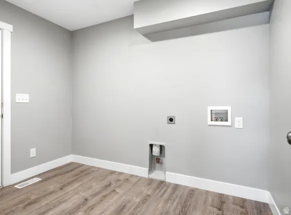 Dedicated laundry area featuring wood-finish flooring, light grey wall paint, white baseboards, and a white door frame