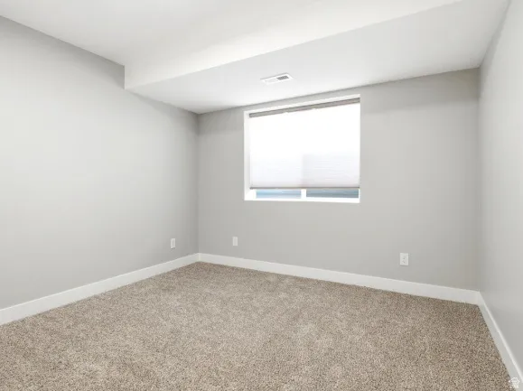 Neutral-toned room featuring a single window with a privacy blind, light gray walls, plush carpet flooring, and white trim