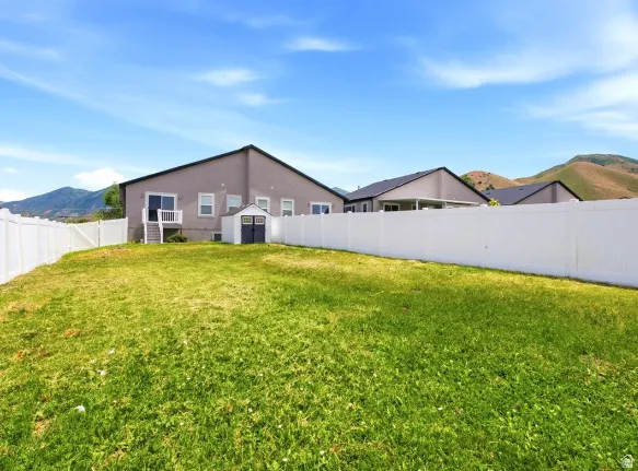Spacious backyard featuring a sloped lawn, white privacy fencing, and a dedicated storage shed