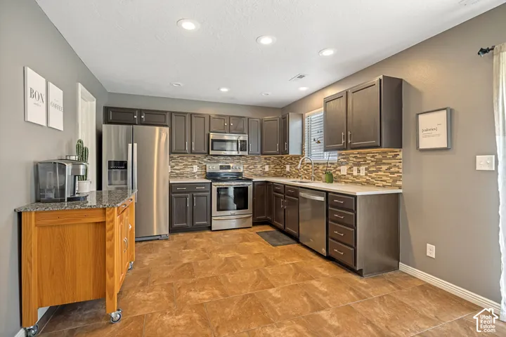 Modern kitchen featuring dark wood cabinetry, stainless steel appliances, a mosaic tile backsplash, light-toned countertops, and recessed lighting