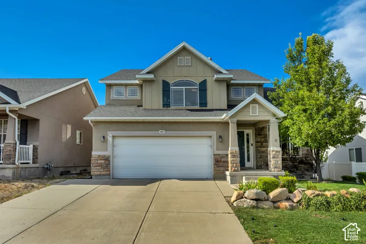 Two-story residence featuring a covered entry, stone veneer accents, an arched window with shutters, a two-car garage, and a concrete driveway