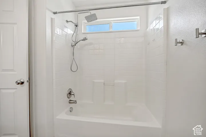 Bathtub and shower combination featuring white subway tile, a rain showerhead, and a separate handheld shower attachment