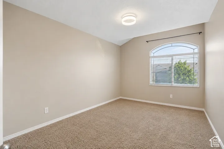 Carpeted room featuring an arched window with blinds, vaulted ceiling, and a flush-mount ceiling light fixture