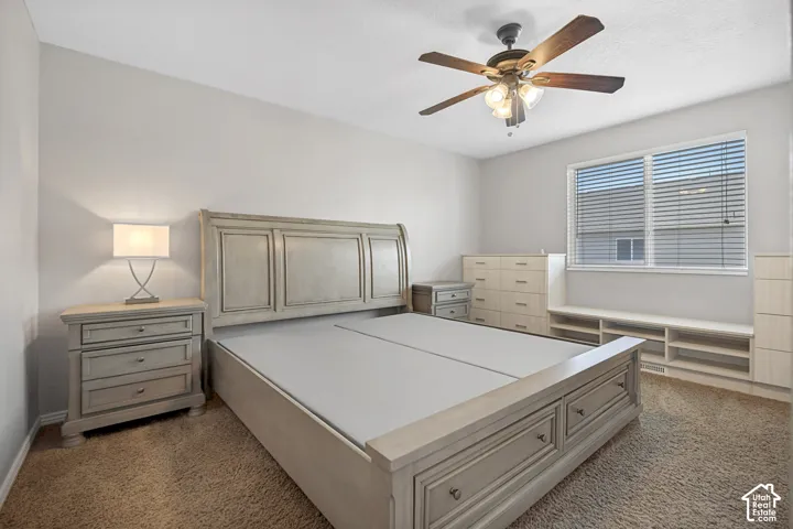 Bedroom featuring light gray walls, brown carpet flooring, and a ceiling fan with integrated lighting