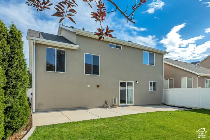 Rear exterior featuring a patio, manicured lawn, stucco siding, and multiple windows