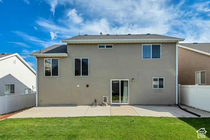 Rear exterior featuring a sliding glass door, multiple windows, a concrete patio, a manicured lawn, and white privacy fencing