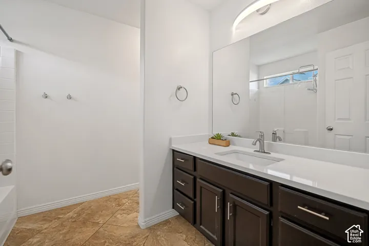 Bathroom featuring a dark wood vanity with a white countertop, an integrated rectangular sink, a large wall-mounted mirror, and tile flooring