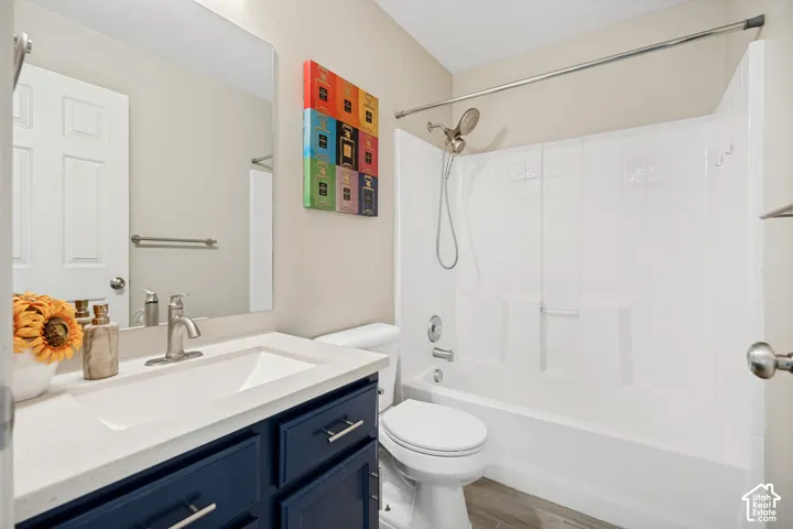 Bathroom featuring a white integrated sink with a light-colored countertop, a navy blue vanity with silver-tone hardware, a rectangular vanity mirror, a white toilet, and a bathtub with a shower head and white surround