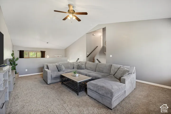 Spacious living area featuring vaulted ceilings, neutral-toned carpeting, and a ceiling fan with integrated lighting