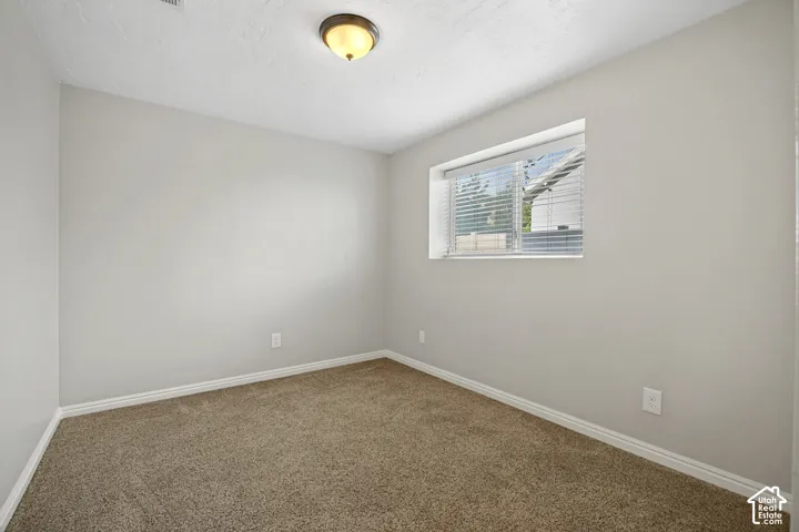 Carpeted room featuring a single window with horizontal blinds, light gray wall paint, white baseboards, and an overhead flush-mount light fixture