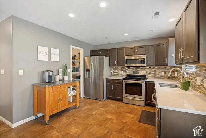 Contemporary kitchen featuring dark wood cabinetry, stainless steel appliances, and a mosaic tile backsplash